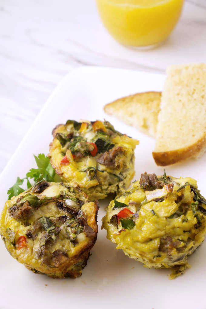 three mini frittatas on a plate with toast and orange juice in the background