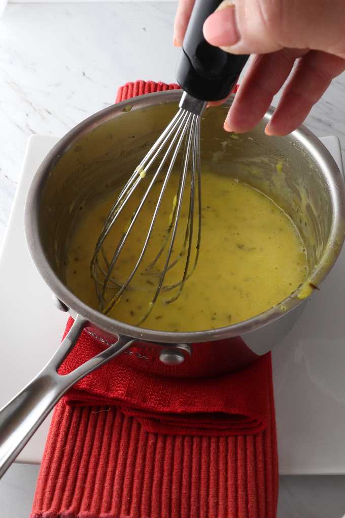 Hollandaise sauce with tarragon being whisked in a pan