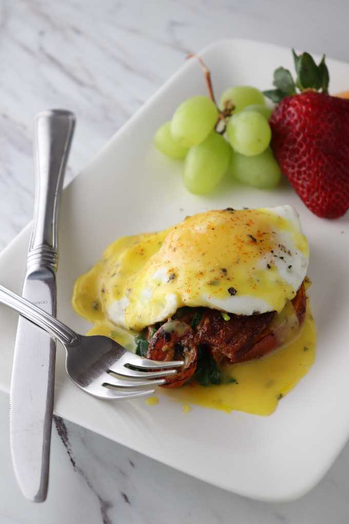 Eggs Benedict with sweet potatoes and hollindaise sause on a plate with fruit